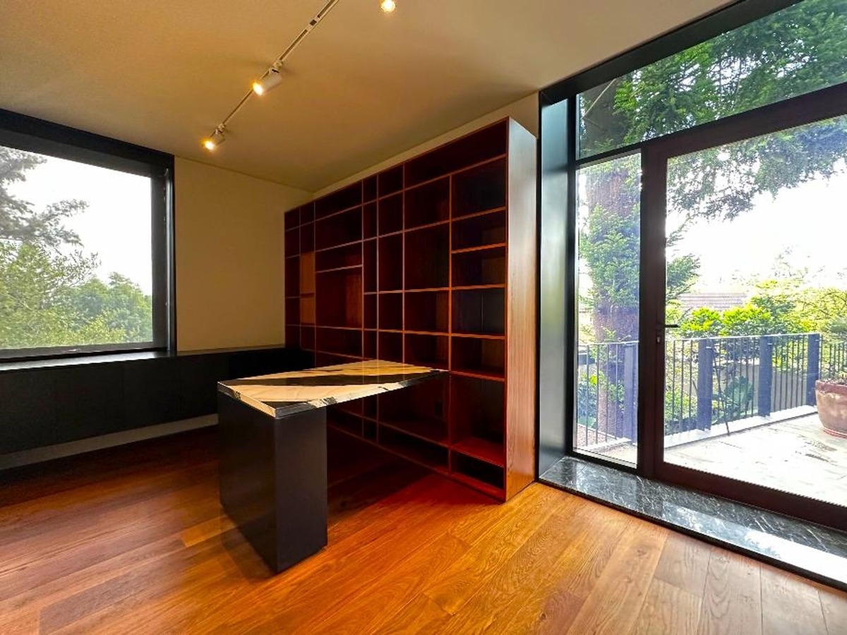 Glass sliding door opening to a balcony with a view of trees and a modern study setup indoors.