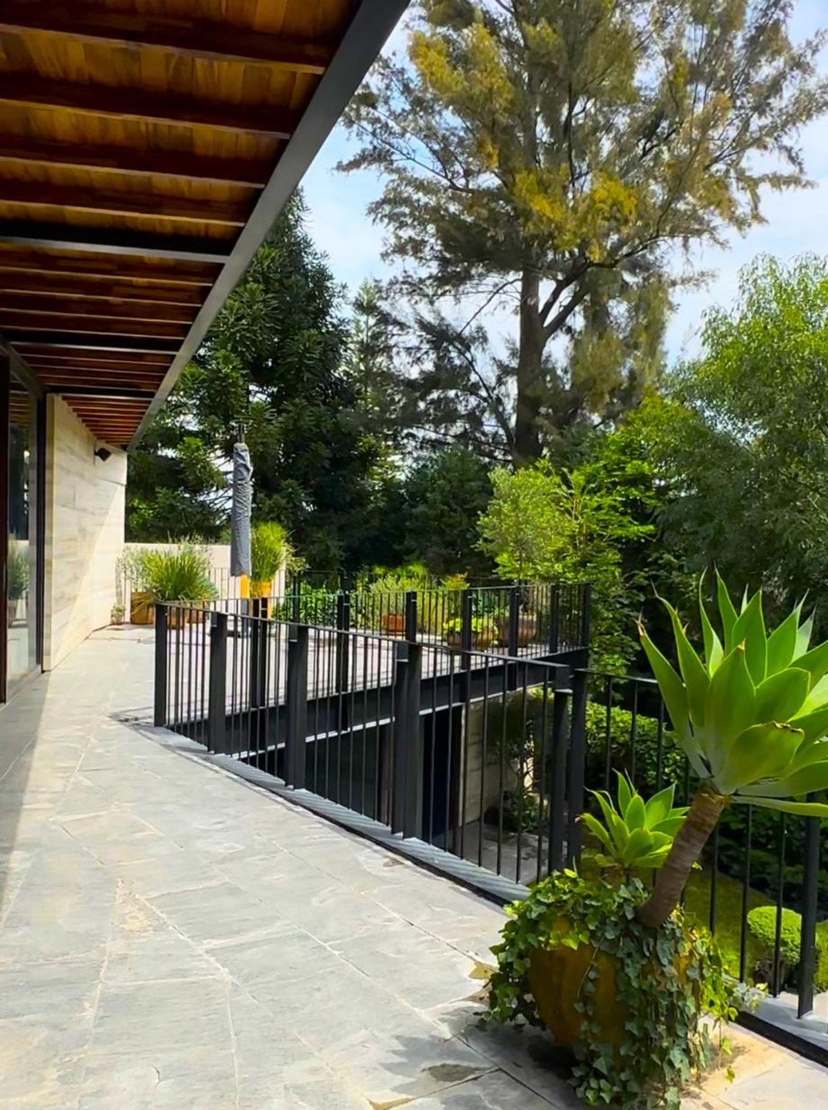 Stone-tiled patio with railing overlooks lush greenery.