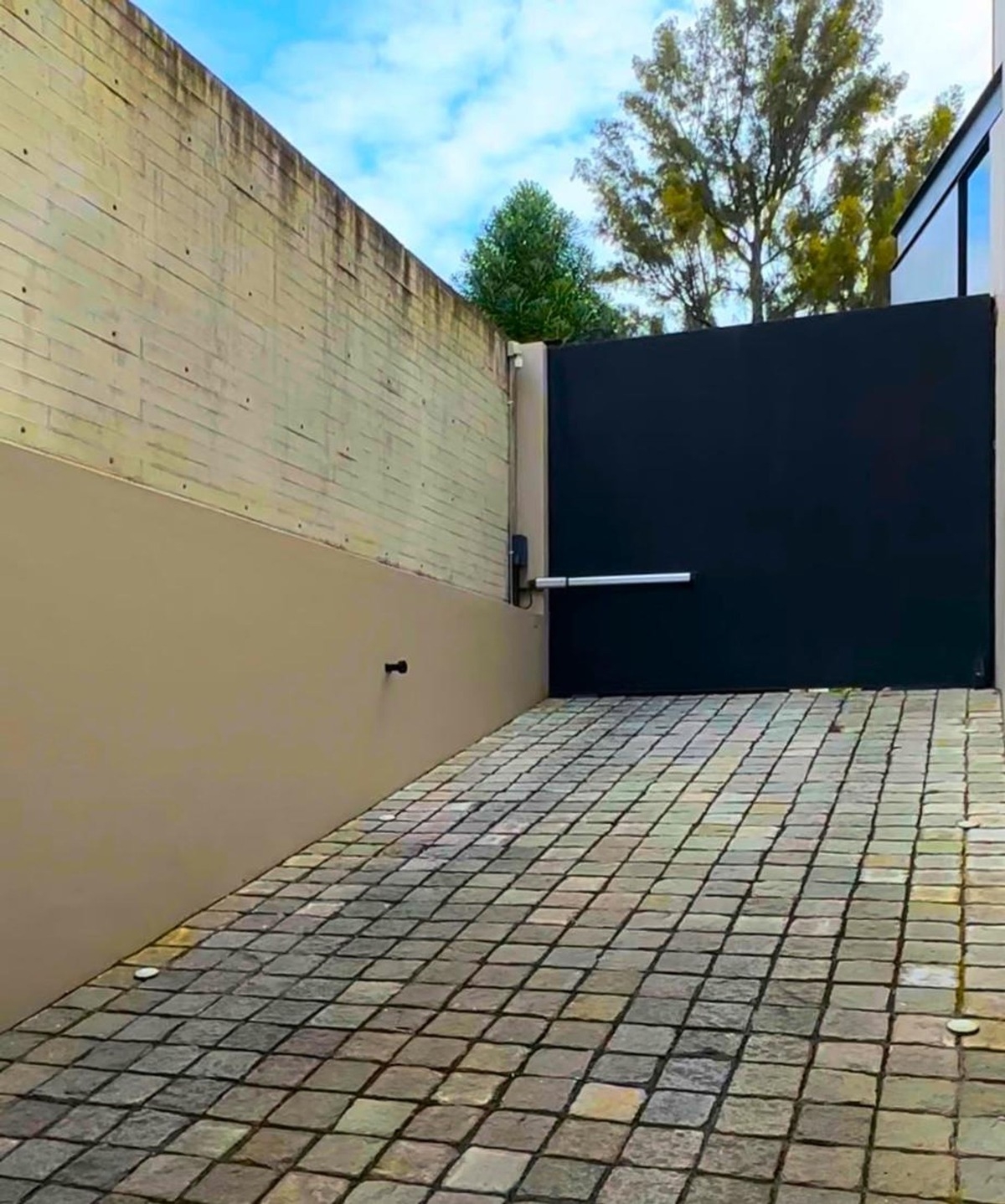 Cobblestone driveway leading to a tall black gate.