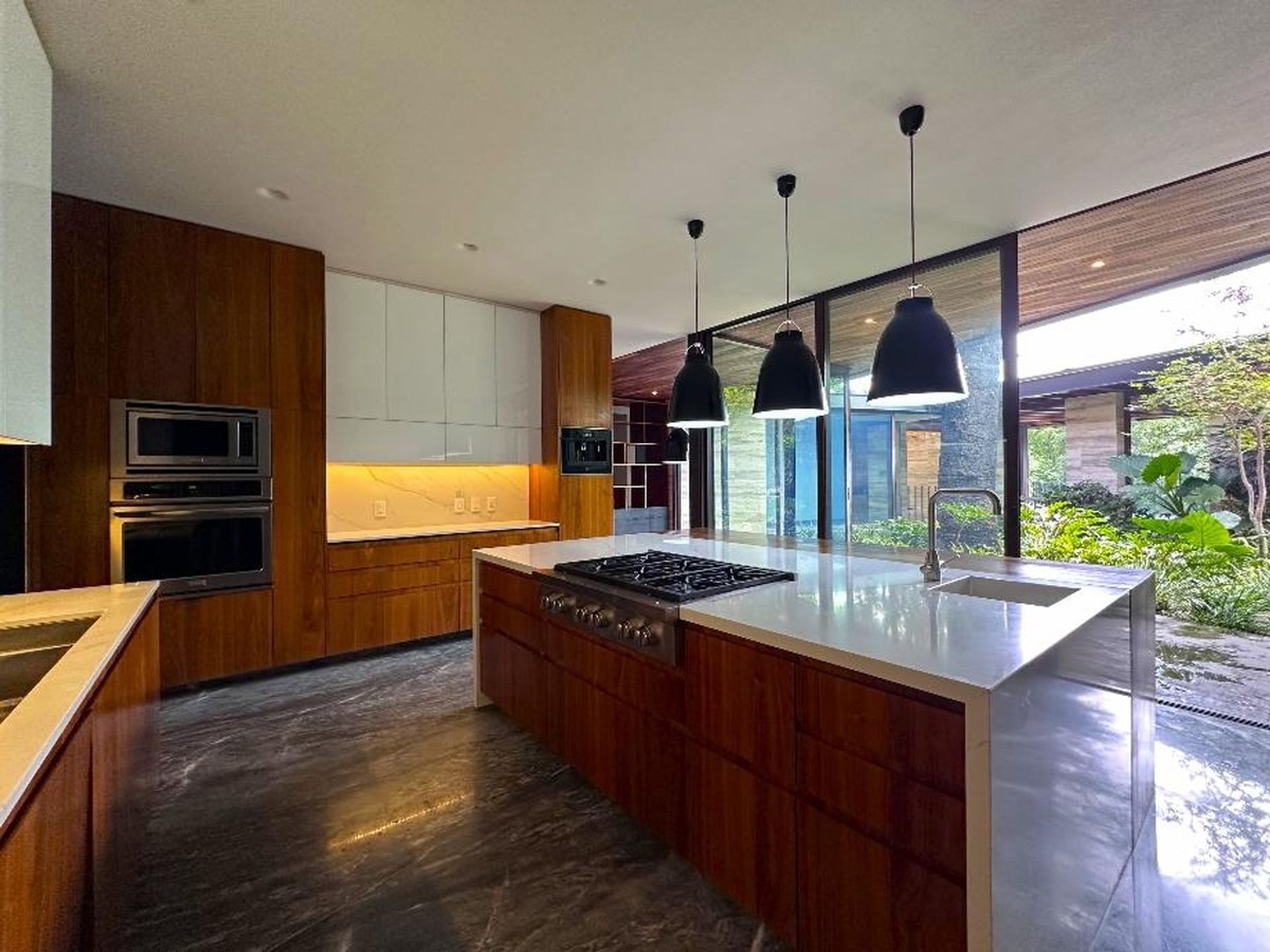 Kitchen interior with wooden cabinetry, marble flooring, and a central island with hanging pendant lights.