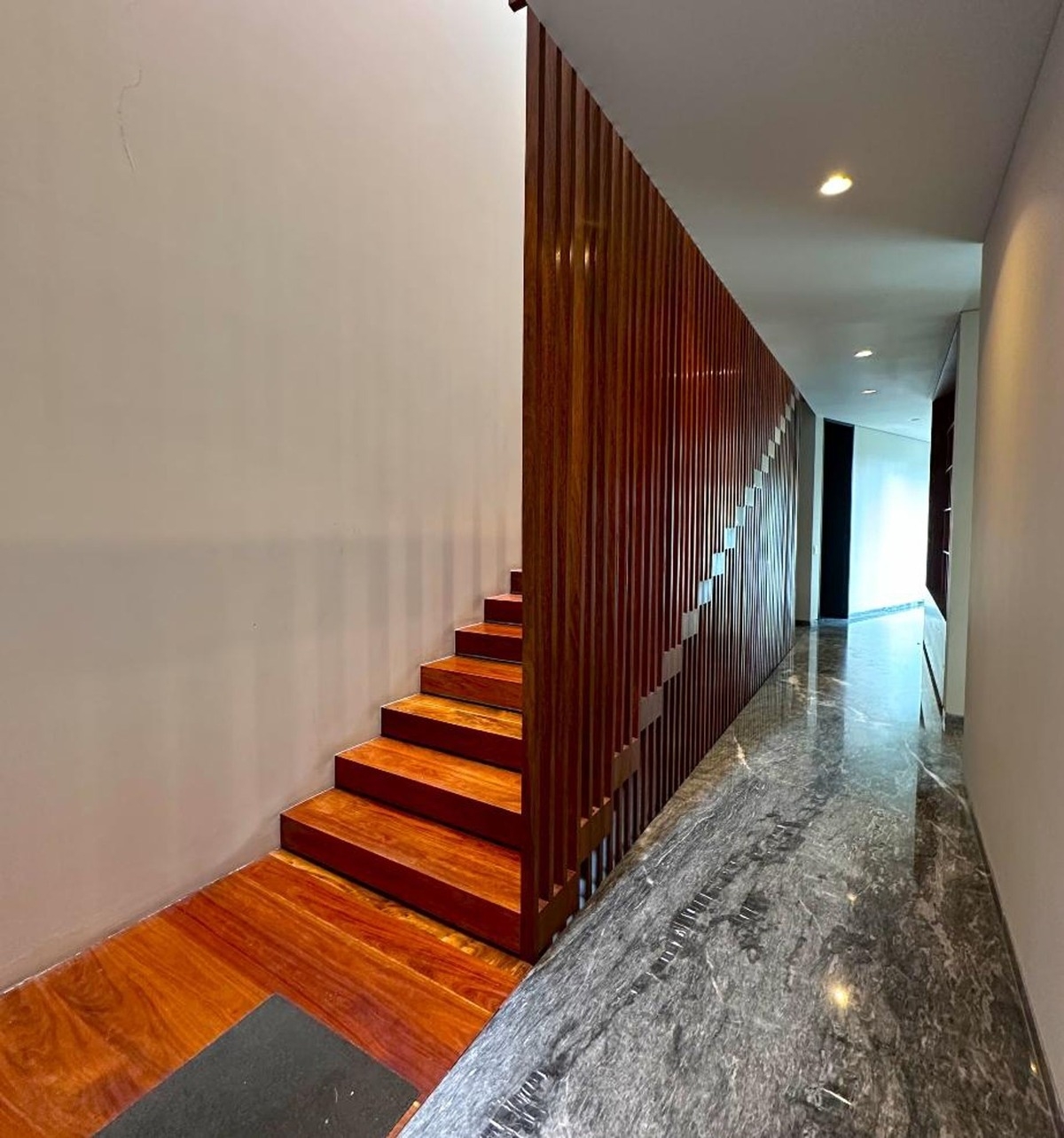 Staircase with wooden steps and a vertical slat design along a polished stone floor.