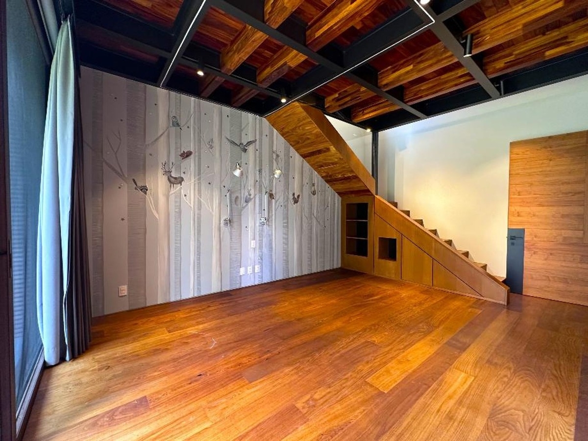 Room with wooden flooring and walls featuring decorative motifs and a staircase leading to a loft.