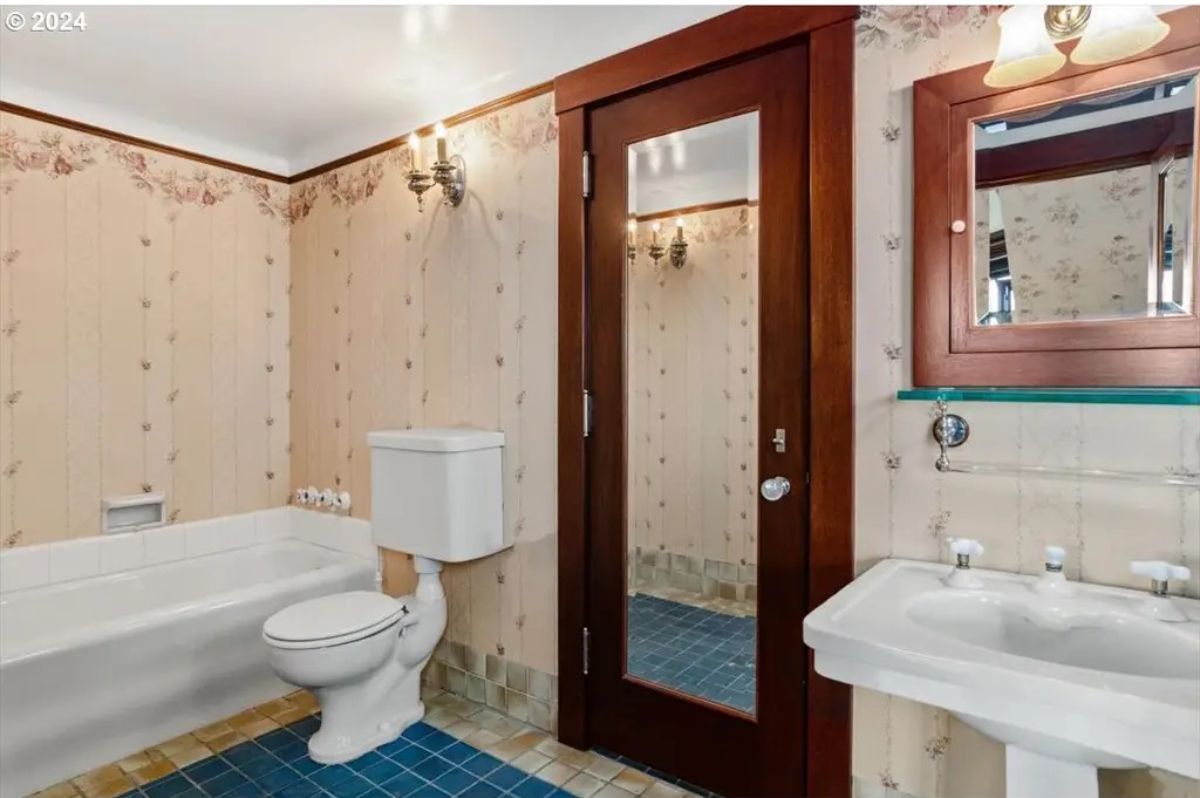 A white bathtub and pedestal sink paired with floral wallpaper.