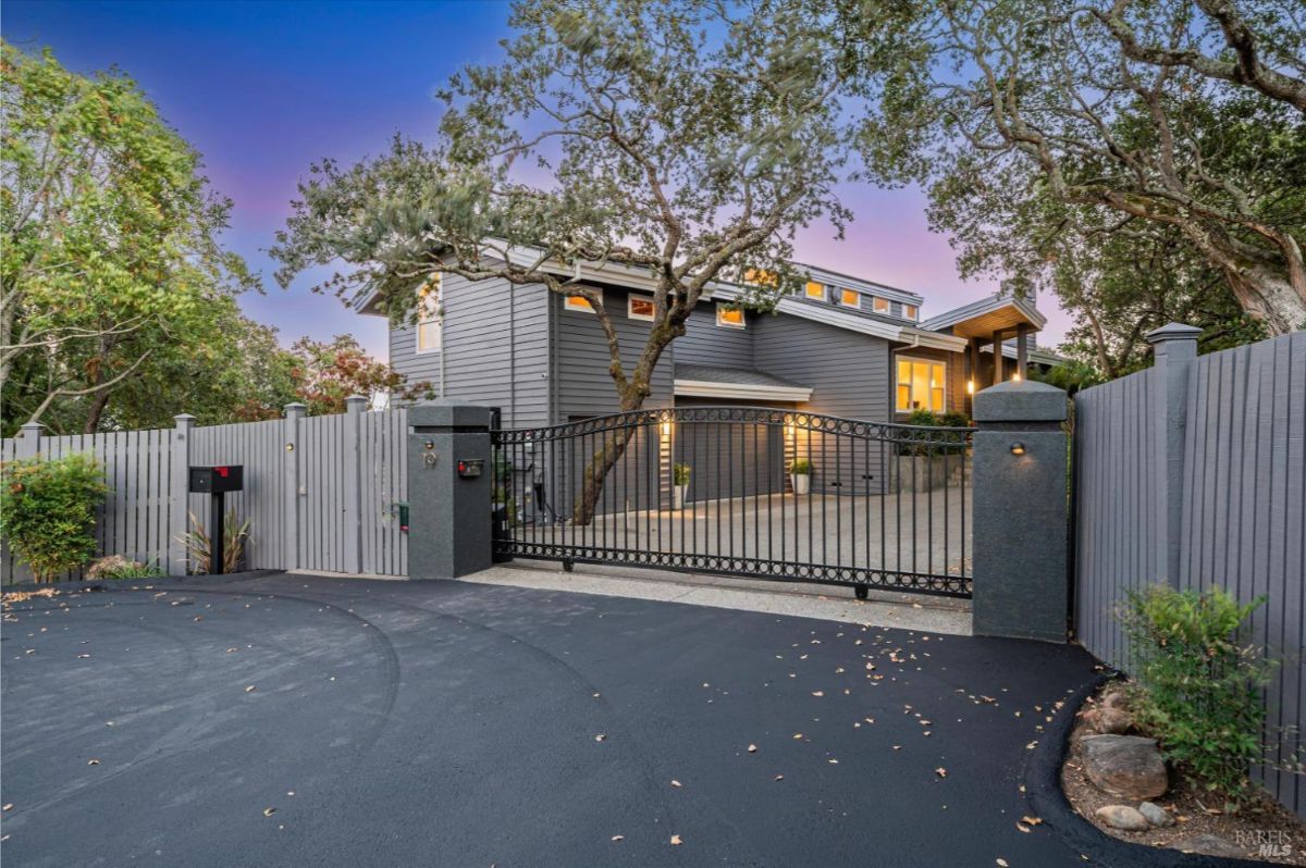 Gated driveway entrance leading to a modern two-story home surrounded by trees.