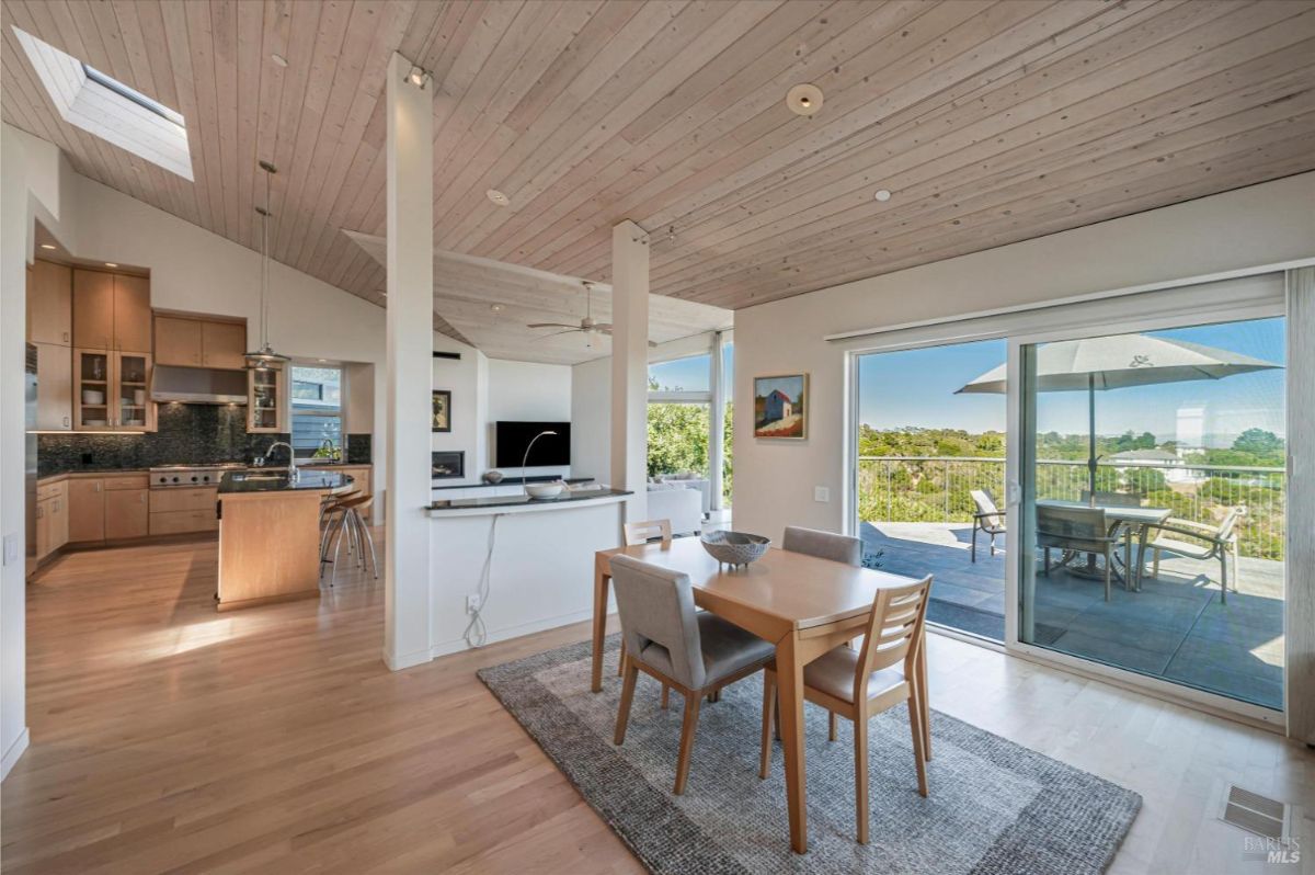 Dining area with sliding doors opening to a deck with outdoor seating and greenery.