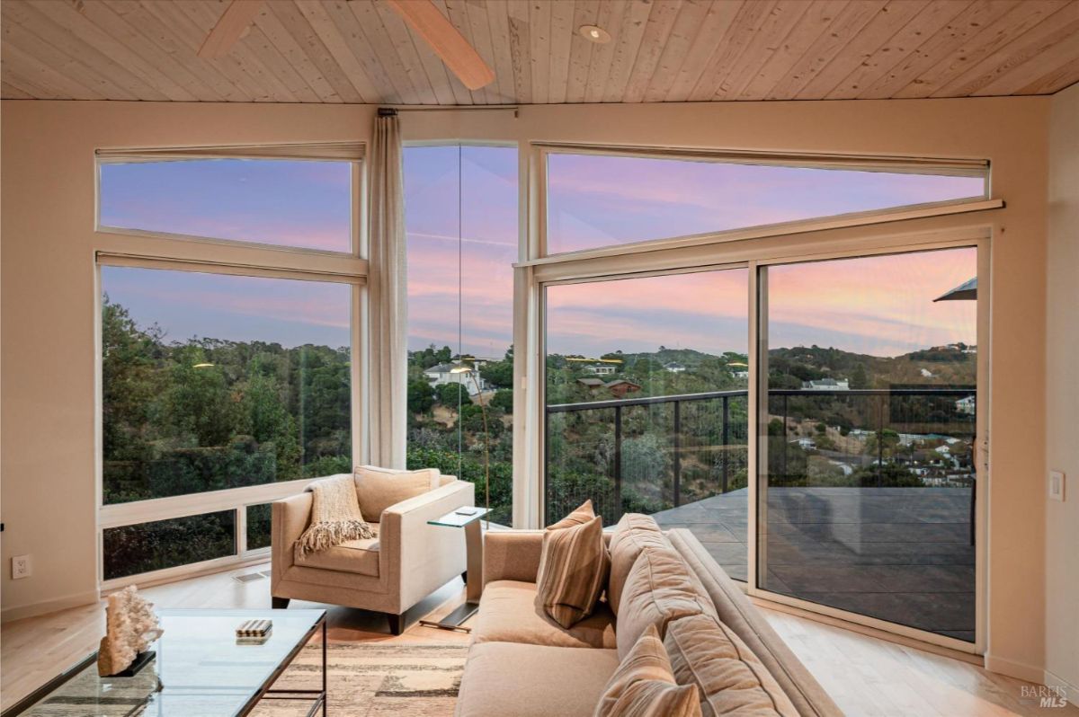 Living room with modern furnishings, glass doors, and a view of a large deck.