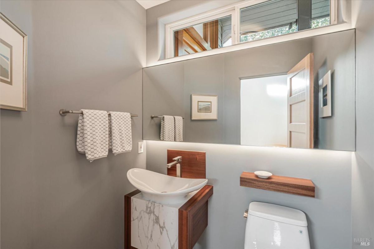 Modern powder room with a floating sink and a mirror above it, a toilet, and a small shelf.