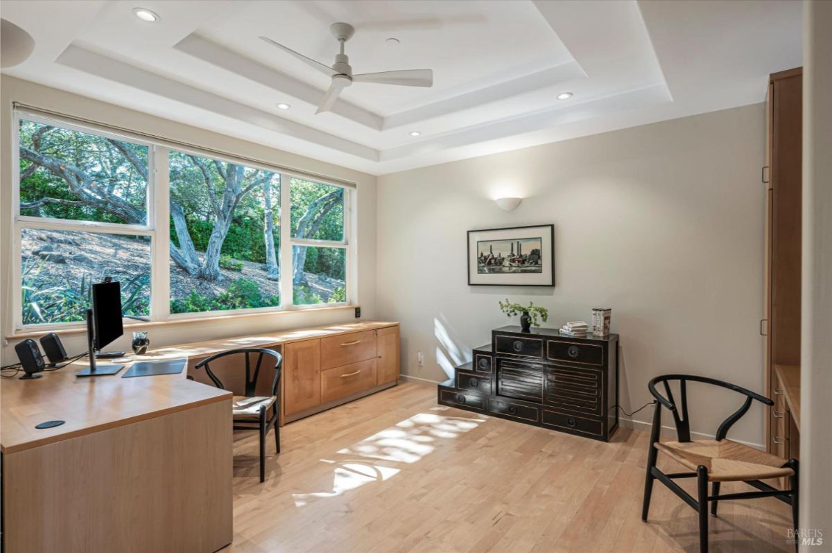 A home office with a desk, drawers, and a large window showcasing greenery outside.