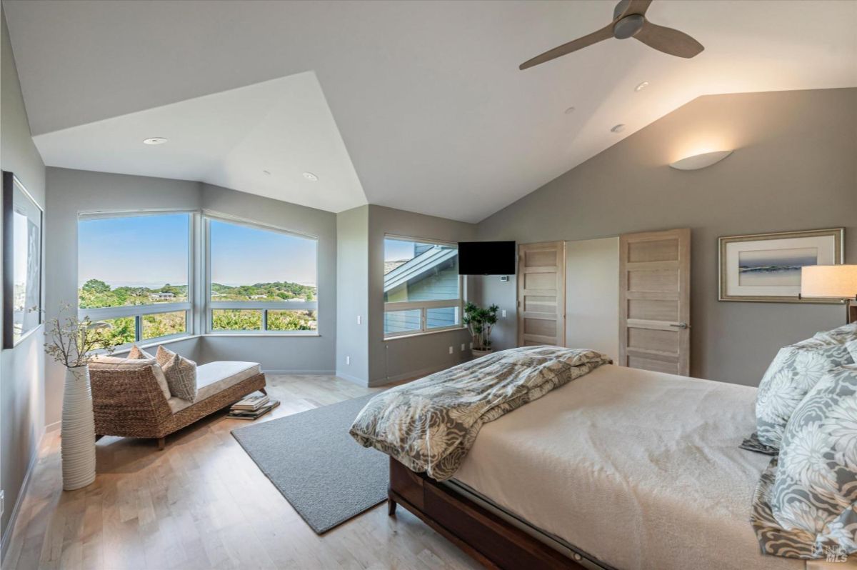 A master bedroom with a sitting area, slanted ceiling, and multiple large windows.