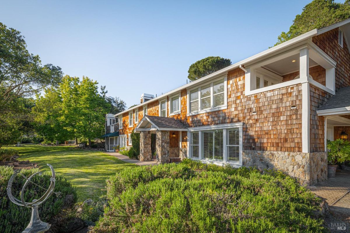 Daytime view of a house surrounded by greenery with stone and shingle siding.