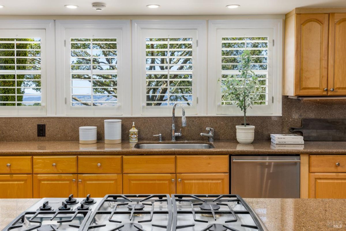 Kitchen stove and sink area with a view of the outdoors through plantation shutters.