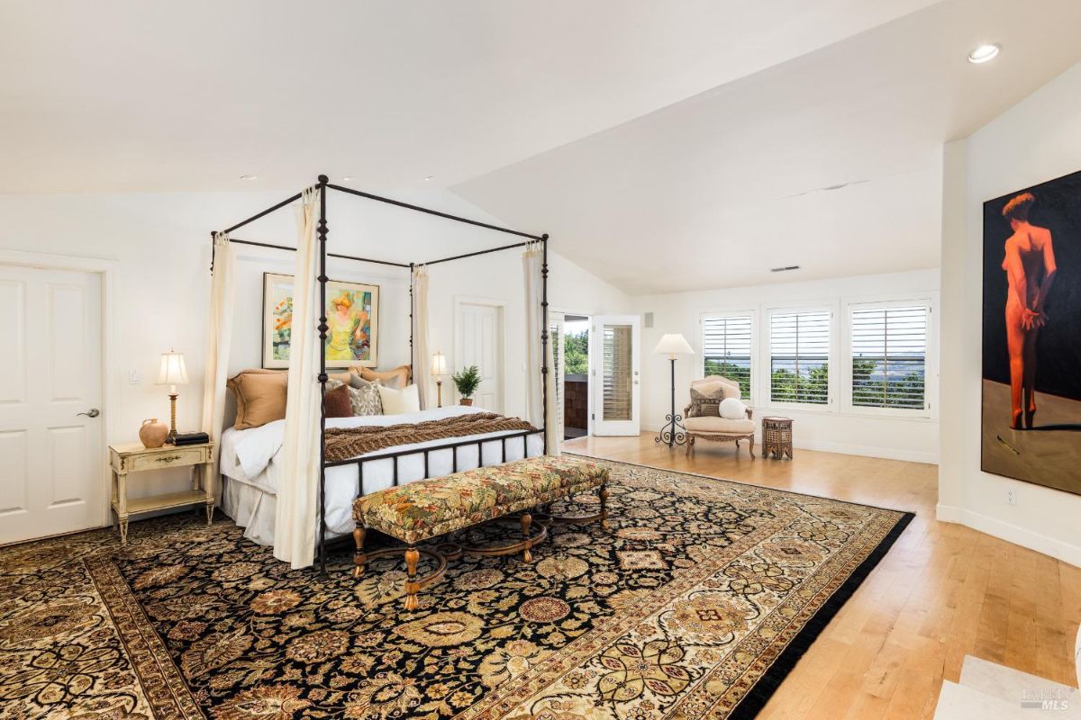 Large bedroom with a canopy bed, patterned rug, and multiple windows.