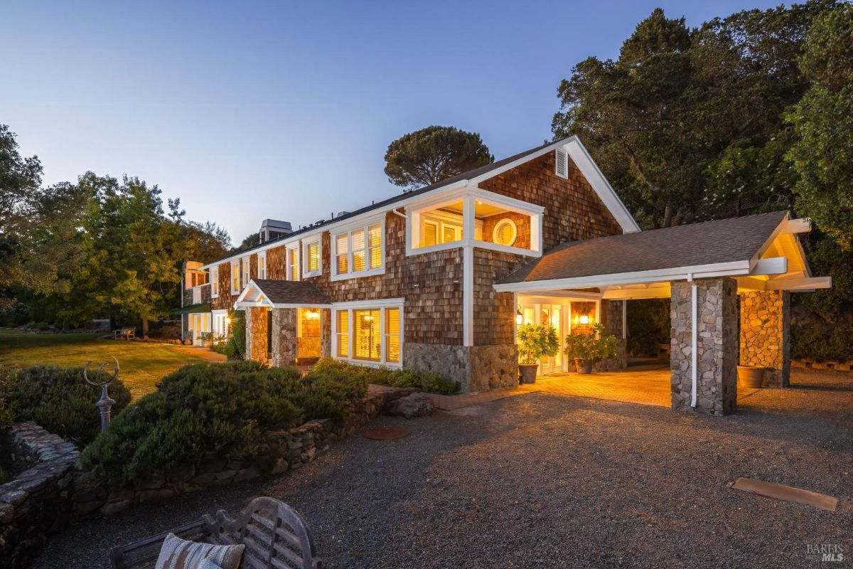 Exterior view of a two-story house with stone and wood siding, illuminated at dusk.