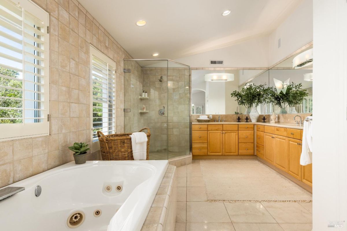 Master bathroom with a glass-enclosed shower, dual vanity, and light beige tiled floors and walls.