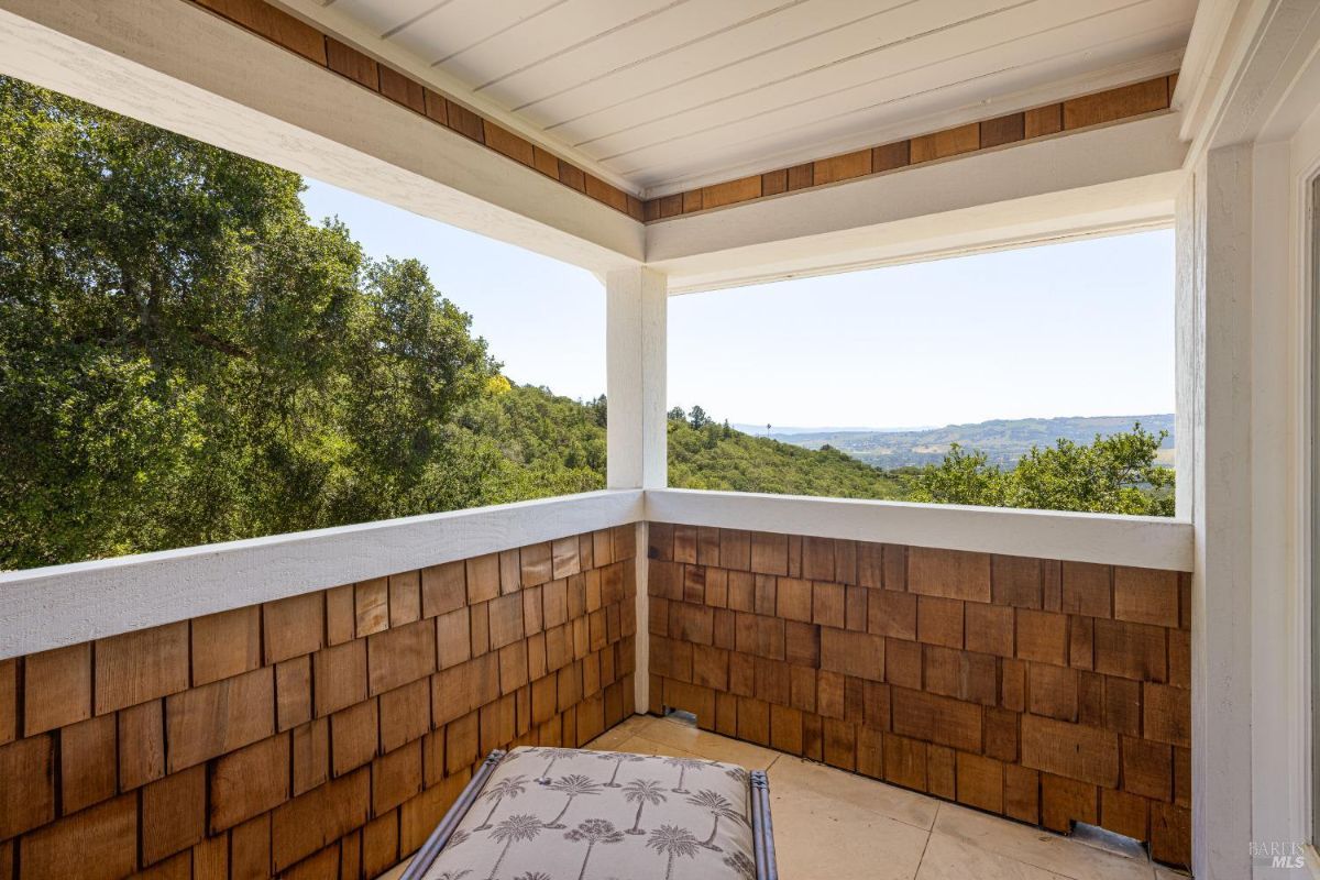 Balcony offers views of greenery and distant hills with wood siding.