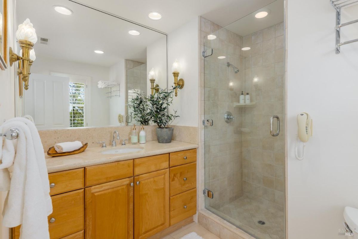 Bathroom features a glass-enclosed shower, double vanity, and beige tiled walls.