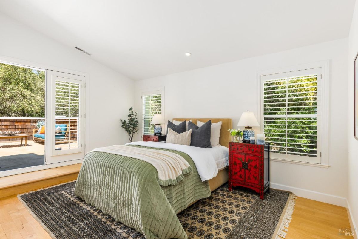 Bedroom with natural light streaming through plantation shutters and a patio door leading to an outdoor deck.