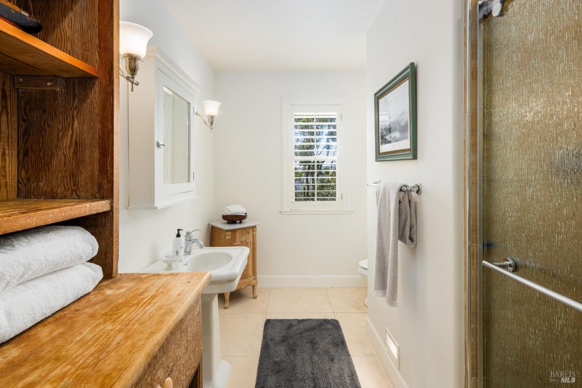 Compact bathroom with wooden shelves, a pedestal sink, and a frosted glass shower door.