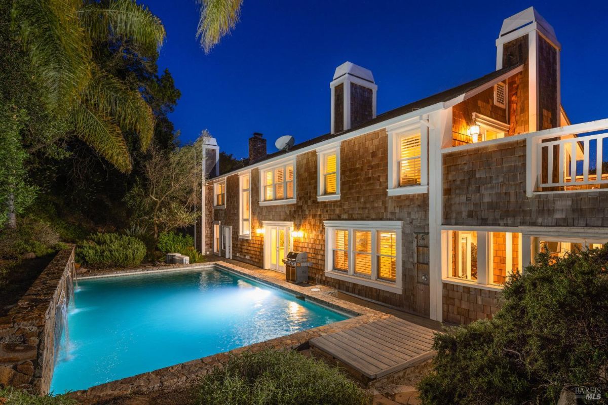 Two-story house with illuminated windows at night and a lit swimming pool.