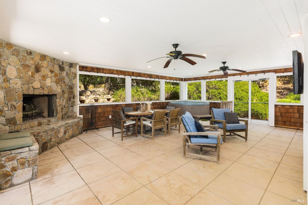 Outdoor patio features a stone fireplace, seating area, and ceiling fans.