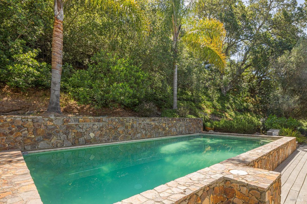 Rectangular swimming pool surrounded by stone walls and lush greenery.