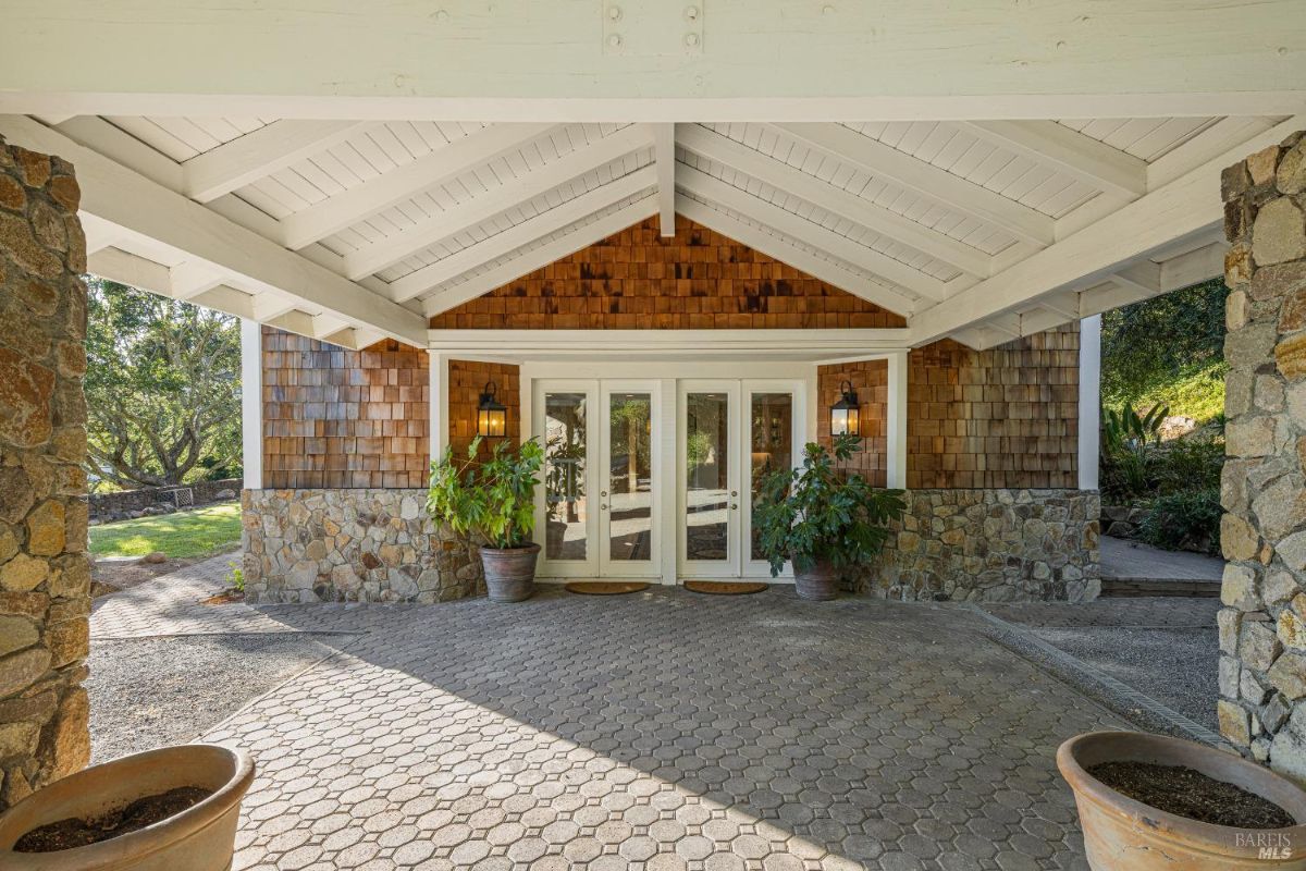 Covered entrance area showcases wood siding, stone walls, and double glass doors.