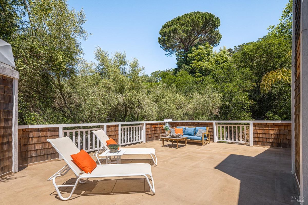 Outdoor deck with lounge chairs, a small table, and surrounding trees.