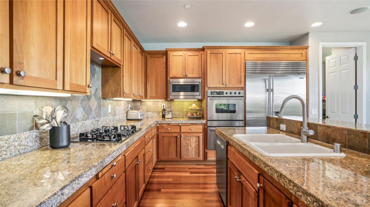 Kitchen showing stainless steel appliances, wooden cabinetry, and dual sinks on granite counters.