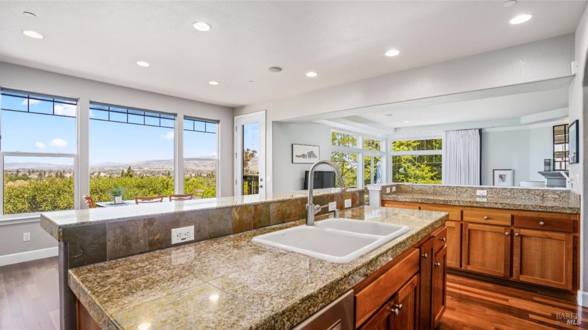 Open kitchen with granite island and expansive windows providing a scenic view of the outdoors.