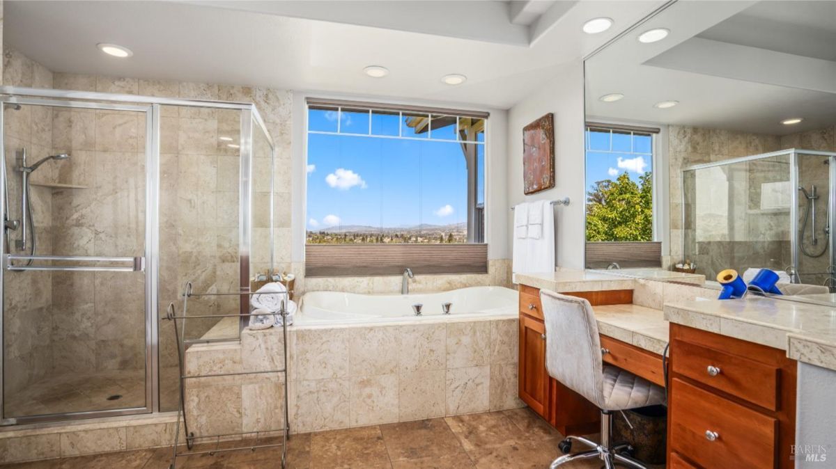 Modern bathroom with a glass shower, soaking tub, and wide mirror reflecting natural light from the window.