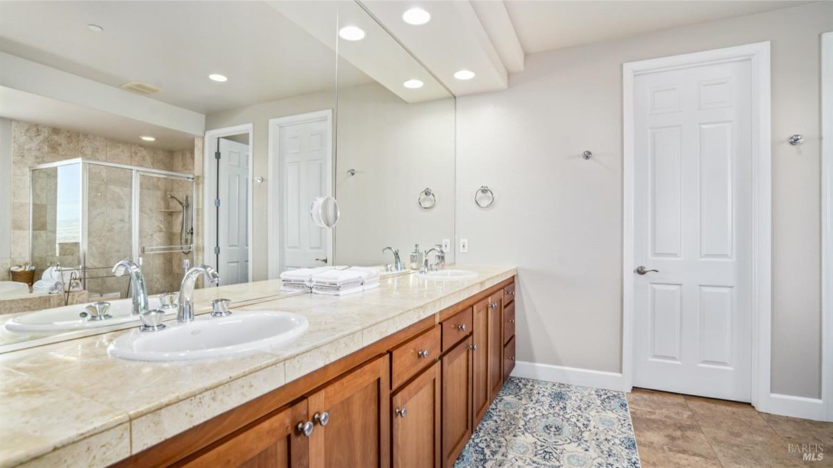 Dual-sink vanity with wood cabinets and tiled countertop in a spacious bathroom.