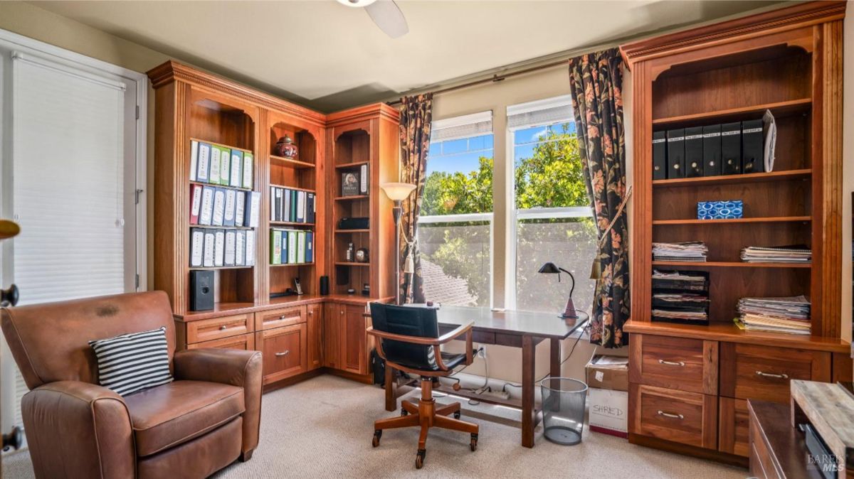 Study or home office with built-in wooden shelves, a desk, and large windows.