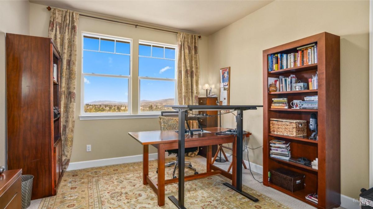 Second office or study space with bookshelves, a large desk, and windows overlooking the outdoors.