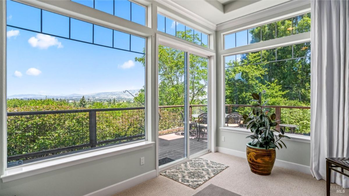 Living room with floor-to-ceiling windows, sliding doors, and views of greenery and a deck.