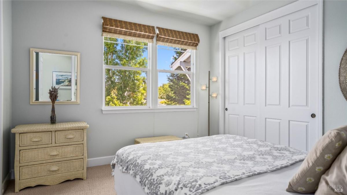 Small bedroom with wicker furniture and large windows overlooking greenery.