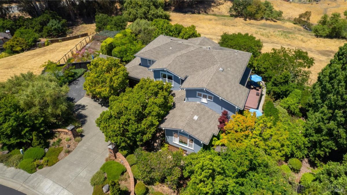 Aerial view of a large two-story house surrounded by gardens and trees, set in a suburban neighborhood.