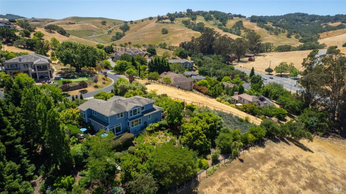 Wide-angle view of a residential area with houses surrounded by open fields and rolling hills.