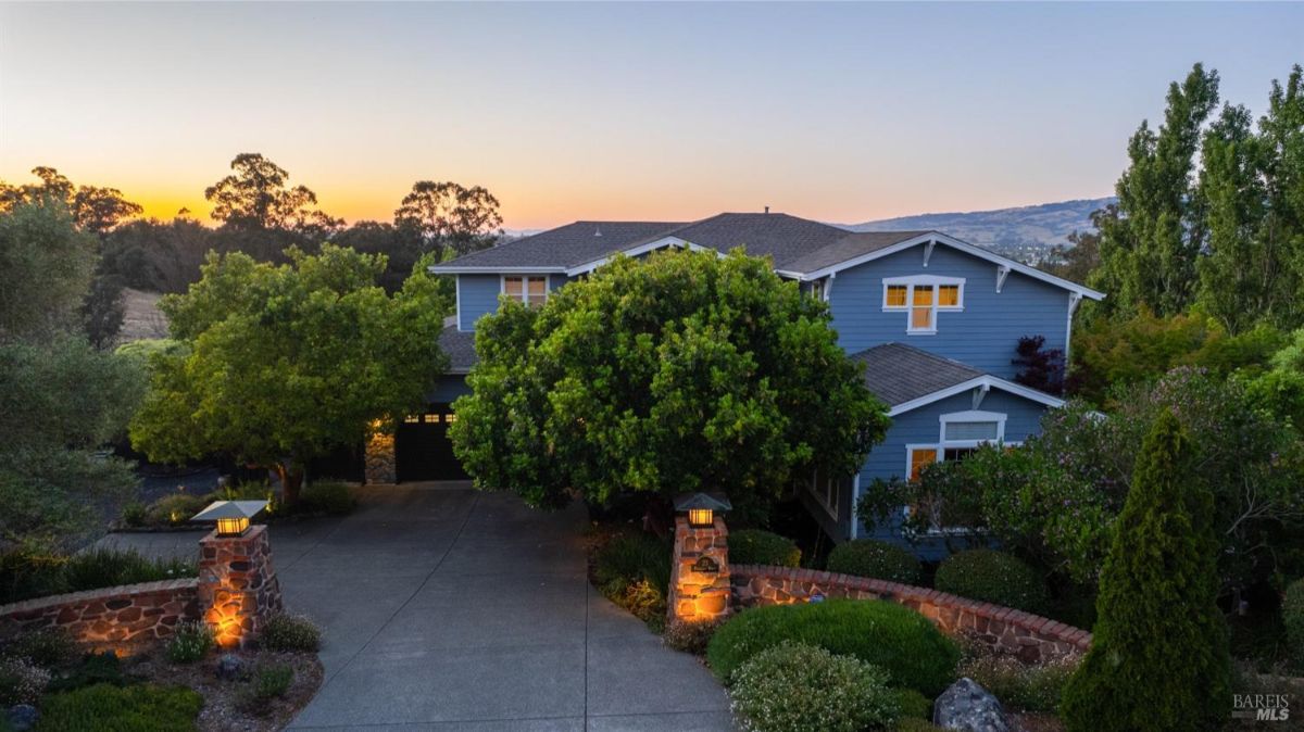 Elevated view of a two-story house surrounded by landscaping and illuminated at dusk.