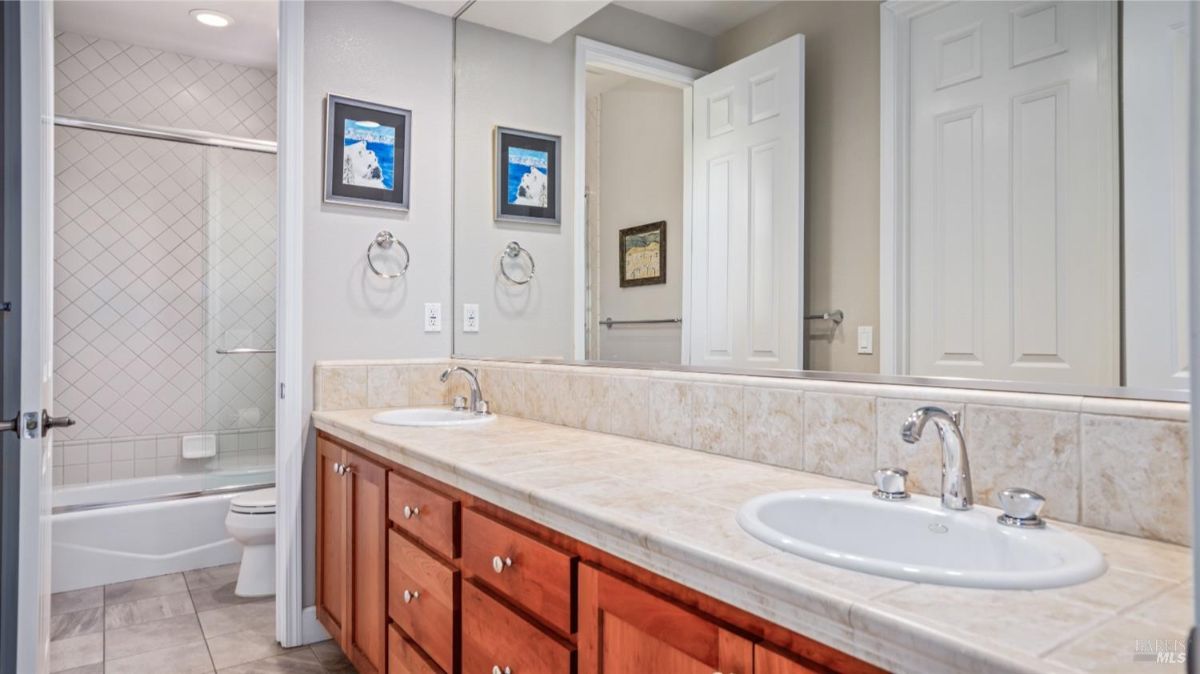 Bathroom with double sinks, a large mirror, and a shower area with tiled walls.