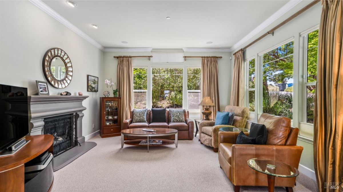 Living room with a fireplace, leather chairs, and a large window overlooking greenery.