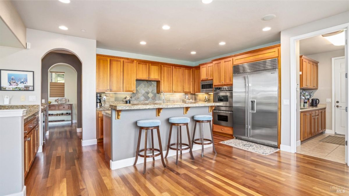 Spacious kitchen area with a bar counter and high stools adjacent to a stainless steel refrigerator.