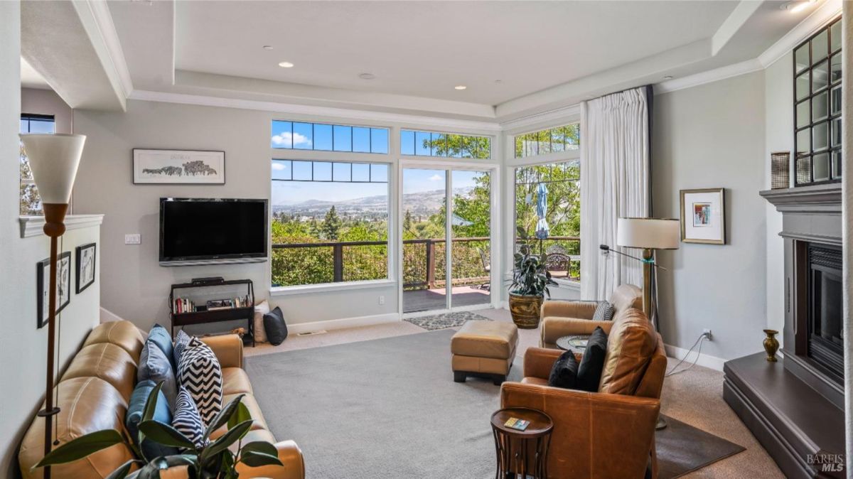 Living room with large windows, a TV, leather seating, and a fireplace.