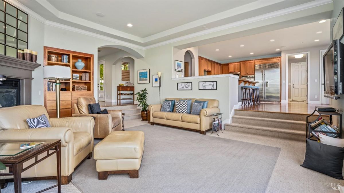 Open-concept living room and kitchen with beige seating, a fireplace, and hardwood cabinets.