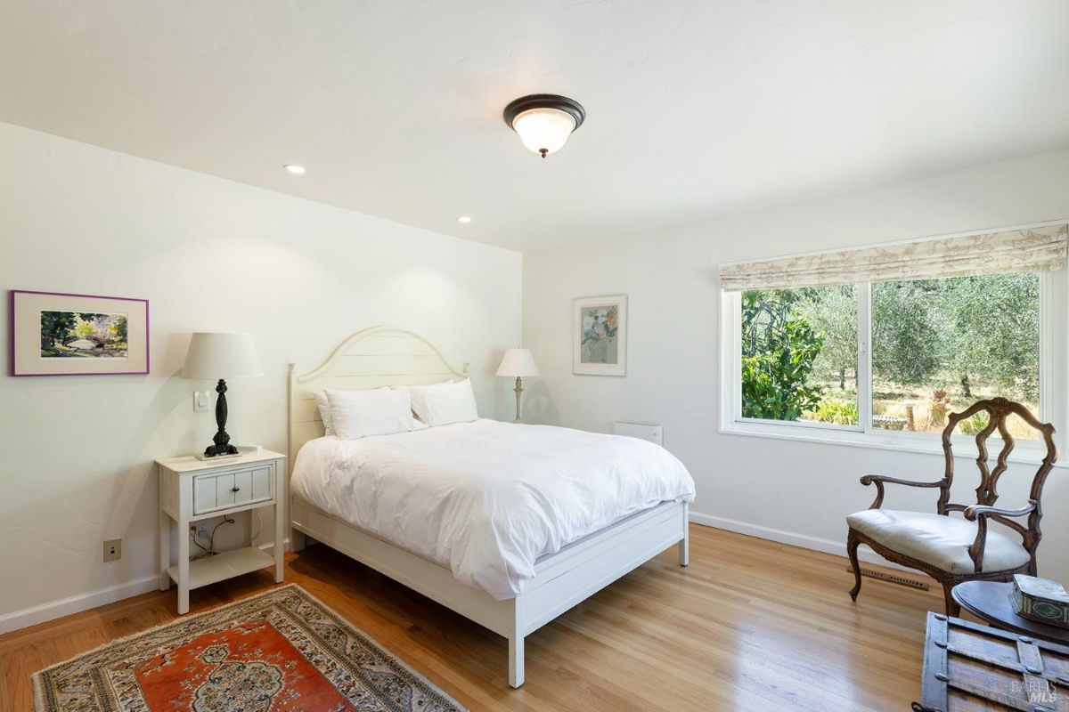 Bedroom with a white bed frame, wood flooring, and a window facing a garden view.