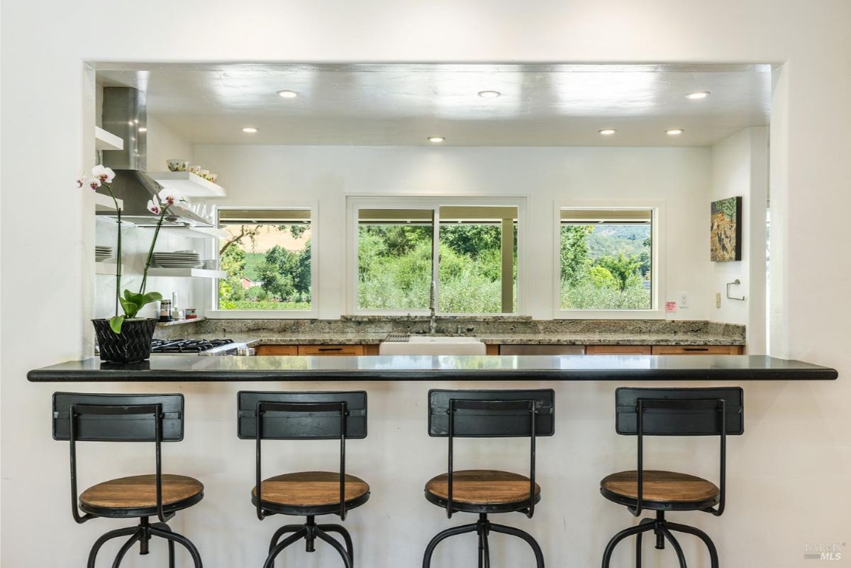 Kitchen counter with four stools, overlooking a window with outdoor views.