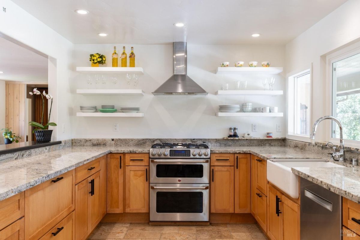 Modern kitchen with granite countertops, open shelving, and a double oven.