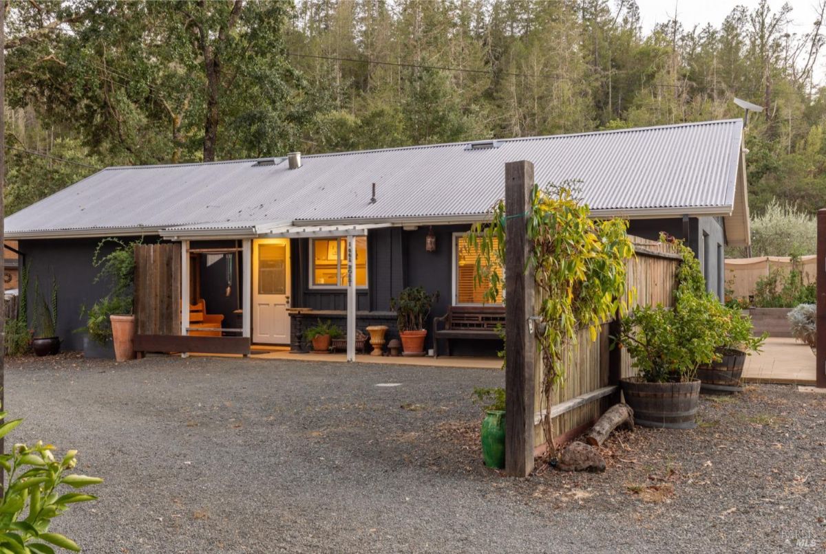 Secondary building has a metal roof, gravel driveway, and fenced garden area.