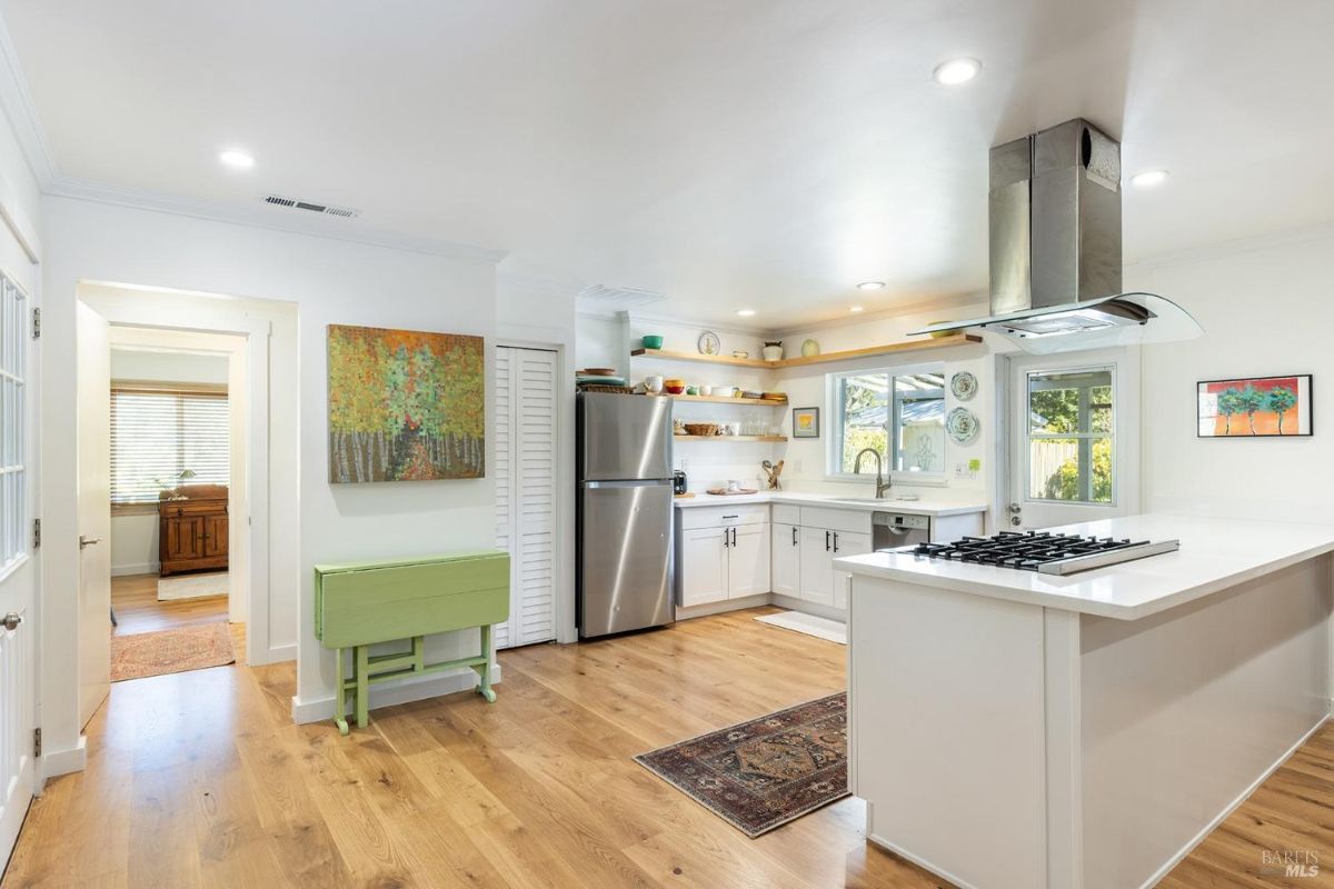 Open kitchen layout with white cabinetry, stainless steel appliances, and wood flooring.