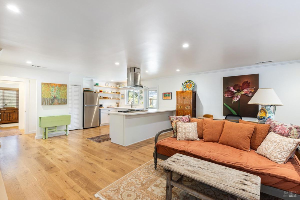 Open-plan kitchen and living area with wood flooring, a large orange couch, and an island with stainless steel appliances.