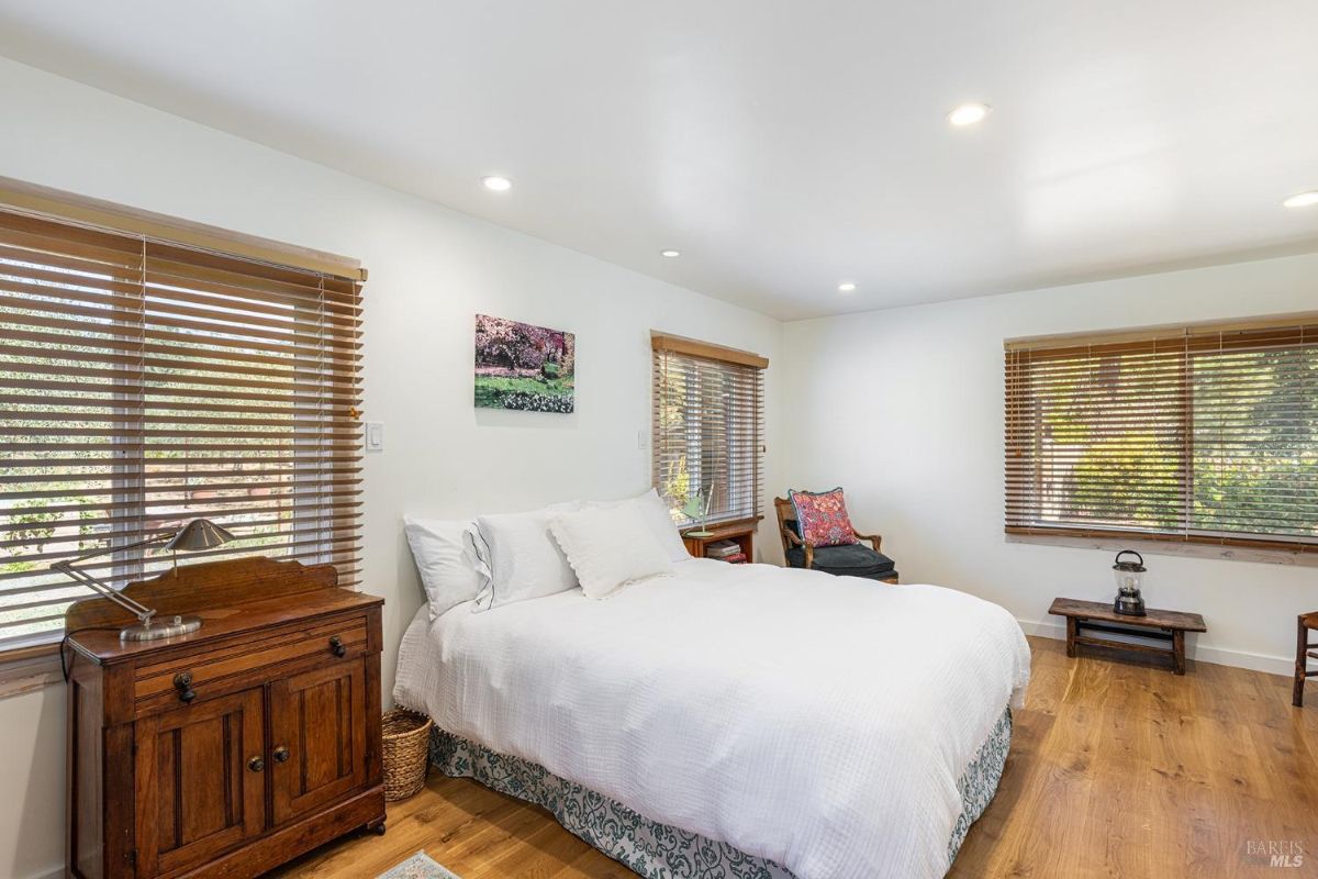 Bedroom with white walls, wooden furniture, and large windows featuring wood blinds.